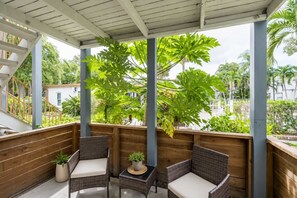 Ein überdachter Außenbereich mit Korbmöbeln und Blumentöpfen, mit Blick auf einen Garten mit großen Bäumen.