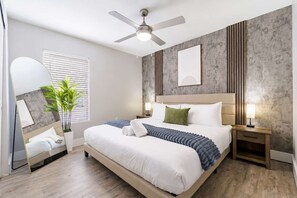 A modern hotel room with a large bed, a ceiling fan, a potted plant, and a large mirror. - South Tampa 2BR | 2 Kings, Pool, Gym & Parking (Tampa)
