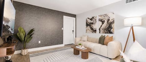 A modern living room with a grey accent wall, a beige sofa, a round black and white rug, and a floor lamp.