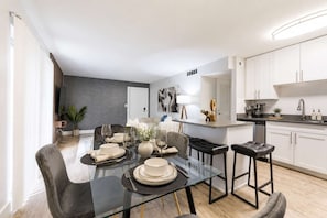 A modern kitchen with white cabinets, a black countertop, and a dining area with a glass table and chairs. - South Tampa 2BR | 2 Kings, Pool, Gym & Parking (Tampa)