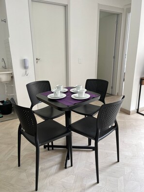 Un comedor con una mesa dispuesta para cuatro, sillas negras, un mantel morado y una pared blanca con una puerta.