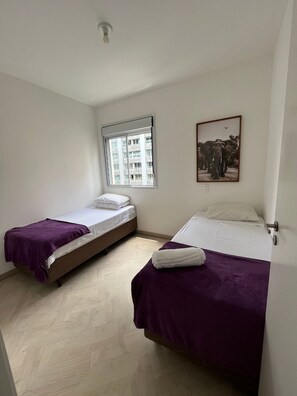 Una habitación con dos camas, un ventanal con vistas a edificios y un cuadro enmarcado en la pared.