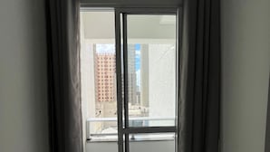 A room with a sliding glass door leading to a balcony, a view of buildings outside, and a light-colored floor. - LK Centro 7 (Belo Horizonte)