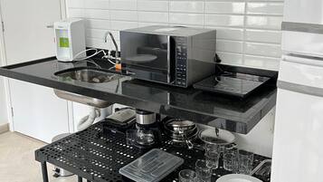 Una cocina con microondas, cafetera y jarra para café sobre una encimera negra.