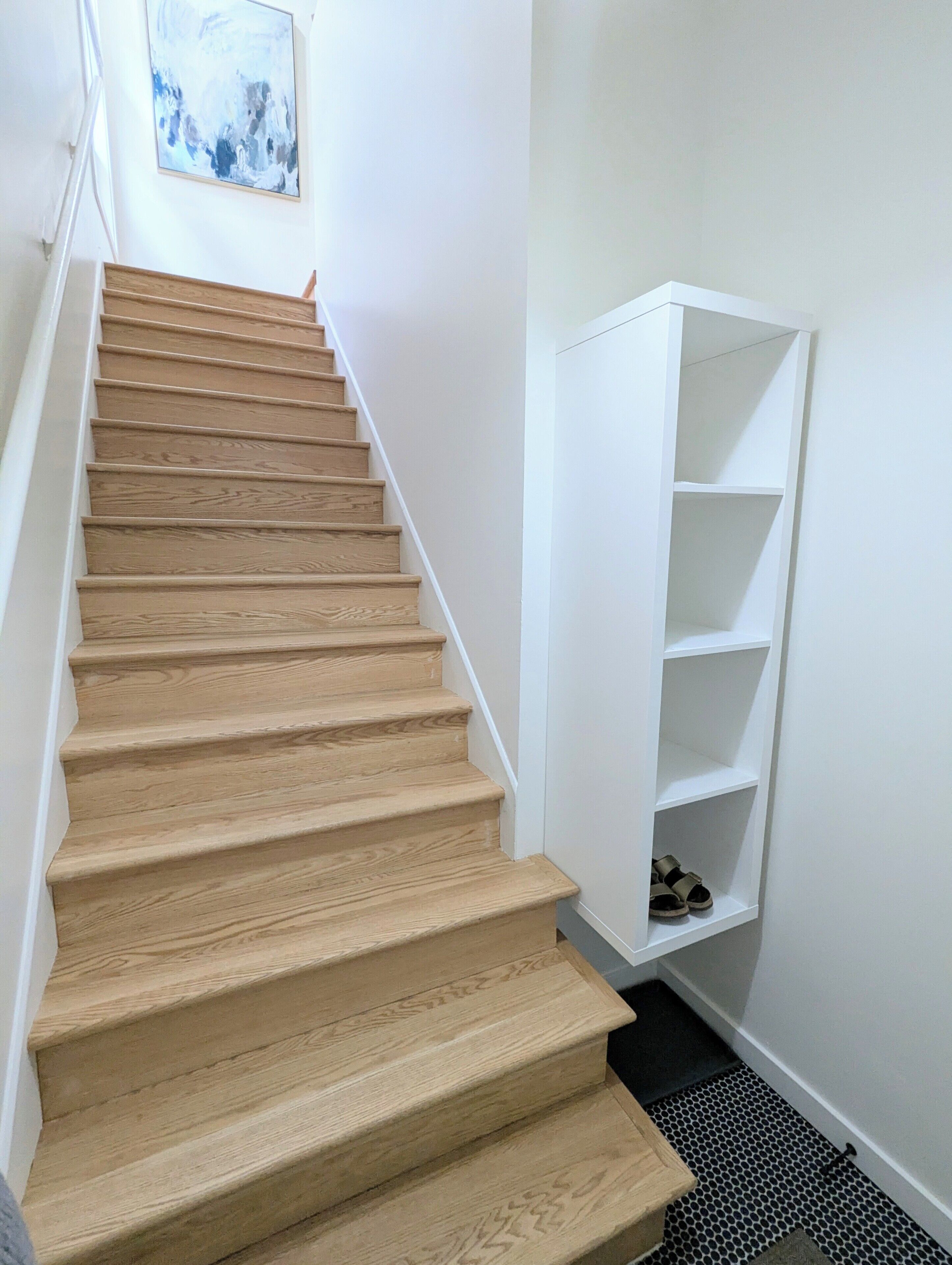 A wooden staircase with white walls and a white shelving unit.