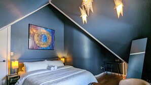 A bedroom with a sloped ceiling, a bed with white linens, a wall-mounted painting, and two star-shaped wall lights. - Modern Victorian Loft 4-bedroom duplex in Saint Paul's central Cathedral Hill (Saint Paul)