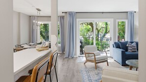 Una sala de estar moderna con comedor, ventanas amplias con cortinas, un sofá y un sillón.