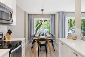 Eine moderne Küche mit Essbereich, großen Fenstern und Blick auf Grünfläche.