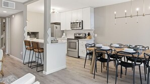 Una cocina moderna con armarios blancos, microondas y un comedor con mesa de madera y sillas negras.