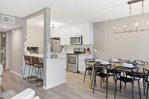 Eine moderne Küche mit weißen Schränken, einer Mikrowelle und einem Essbereich mit einem Holztisch und schwarzen Stühlen.