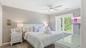Un dormitorio con cama, mesitas de noche, ventilador de techo, televisor y ventana con vistas.