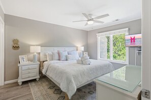 Ein Schlafzimmer mit Bett, Nachttischen, Deckenventilator, Fernseher und einem Fenster mit Blick.