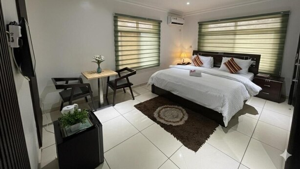 A bedroom with a bed, bedside tables, a desk, a chair, and a small plant.