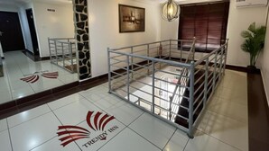 A hotel lobby with a mirrored wall, a staircase, a stone accent wall, and a logo on the floor.