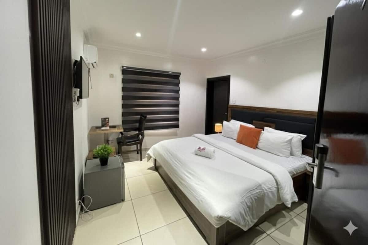 Una habitación de hotel moderna con cama, mesita de noche, una silla y un escritorio pequeño con una planta.