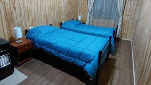 A room with two beds, wooden walls, a ceiling fan, and a nightstand with a lamp.