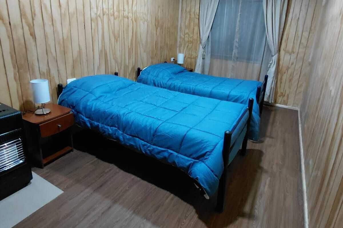 A room with two beds, wooden walls, a ceiling fan, and a nightstand with a lamp.