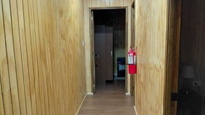 A hallway with wooden walls and a wooden floor, leading to a room with a fire extinguisher mounted on the wall.