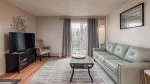 Ein Wohnzimmer mit einer Couch, einem Couchtisch, einem Fernseher und einem Fenster mit Vorhängen.
