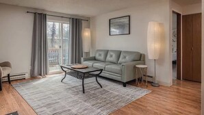 Ein Wohnzimmer mit Sofa, Couchtisch, Lampe und Blick durch eine Glastür.