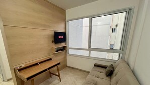 A room with a wooden wall unit, a TV, a sofa, and a window. - LK Centro 8 (Belo Horizonte)