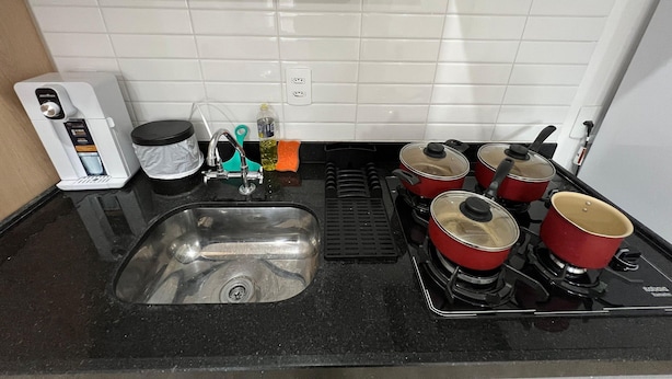 Una cocina con un lavamanos, una cafetera, una estufa con ollas y una encimera.