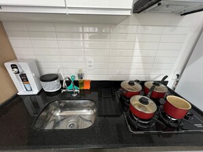 A kitchen with a sink, a coffee maker, a stove with pots, and a countertop. - LK Centro 8 (Belo Horizonte)