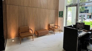 A reception area with a wooden slat wall, two wooden chairs, a bench, a reception desk with a computer, and a glass door leading outside. - LK Centro 8 (Belo Horizonte)