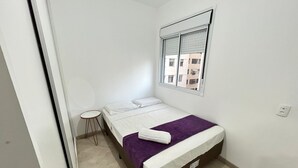 Habitación pequeña con cama individual, ventana, una mesita y toma de corriente visible.