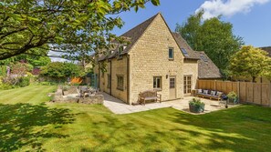 Une maison en pierre avec un patio, un banc en bois et un jardin.