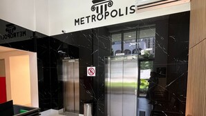 A modern reception area with a sign reading 'METROPOLIS,' a trash bin, an elevator, and a seating area with chairs. - LK Centro 9 (Belo Horizonte)