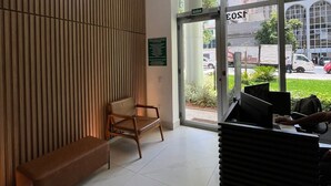 A reception area with a wooden panel wall, a single wooden chair, a glass door with a sign, and a desk with a computer. - LK Centro 9 (Belo Horizonte)
