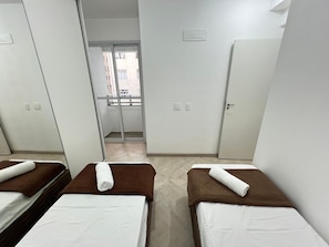 A hotel room with two beds, a wardrobe, a door, and a view of a balcony.