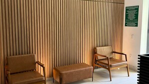 A reception area with a wooden slatted wall, two leather chairs, a bench, and a sign on the wall. - LK Centro 9 (Belo Horizonte)