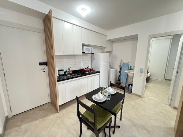 A compact kitchen with white cabinets, a black countertop, and a dining table with chairs.