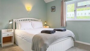 A bedroom with a bed, bedside tables, a nightstand, a window with curtains, and a wall-mounted light fixture. - NEW Family Home in Whitstable | Pets Welcome (Whitstable)