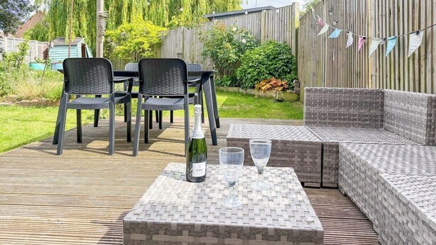 An outdoor patio with a table, chairs, and a cushioned seating area. - NEW Family Home in Whitstable | Pets Welcome (Whitstable)
