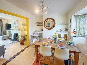 A dining area with a wooden table, white chairs, and a round mirror on the wall. - NEW Family Home in Whitstable | Pets Welcome (Whitstable)