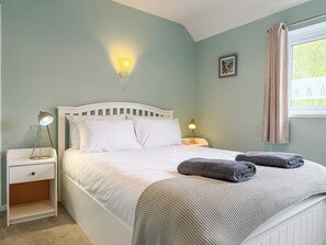 A bedroom with a bed, bedside lamps, a nightstand, a window with curtains, and a wall-mounted light fixture. - NEW Family Home in Whitstable | Pets Welcome (Whitstable)
