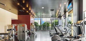 Ein Fitnessraum mit Cardiogeräten, Gewichten und großen Fenstern mit Blick ins Freie.