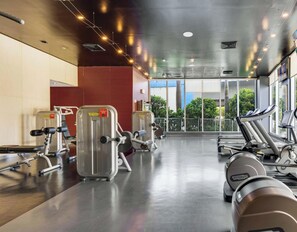 Ein Fitnessraum mit Cardiogeräten, Gewichten und großen Fenstern mit Blick ins Freie.