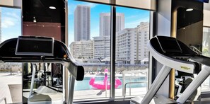 Ein Fitnessraum mit Trainingsgeräten und einem großen Fenster mit Blick auf die Stadt.