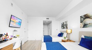 Une chambre d’hôtel équipée d’un bureau, de deux lits, d’une télévision et d’œuvres d’art aux murs.