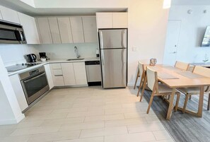 A modern kitchen with stainless steel appliances, a dining area with a wooden table and chairs, and a small potted plant on the wall. - High-Floor 1BR, Intracoastal View, Resort & Pool (Hallandale Beach)