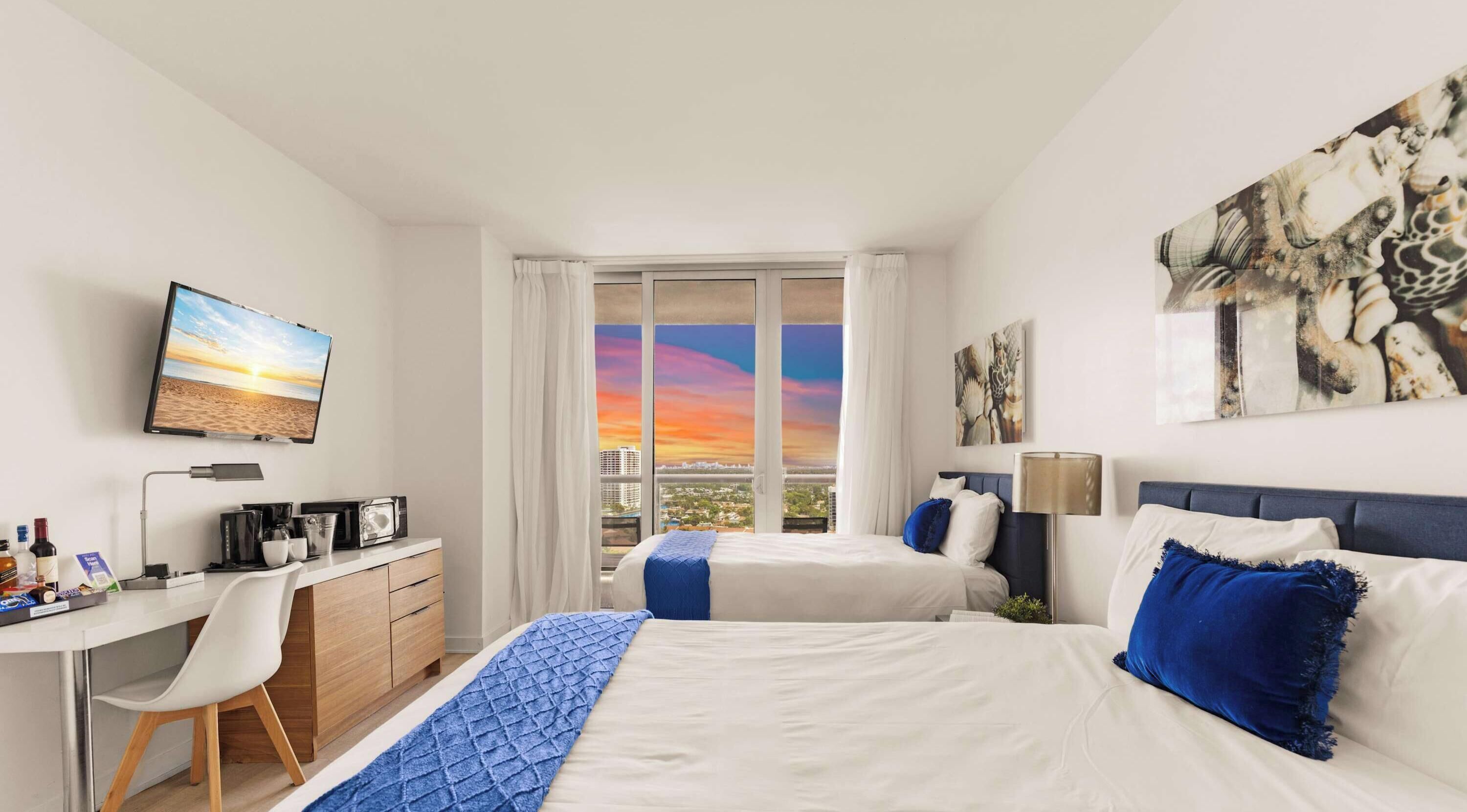 Une chambre d’hôtel équipée d’un lit, d’un bureau, d’une chaise, d’une télévision et d’une fenêtre donnant sur la ville.