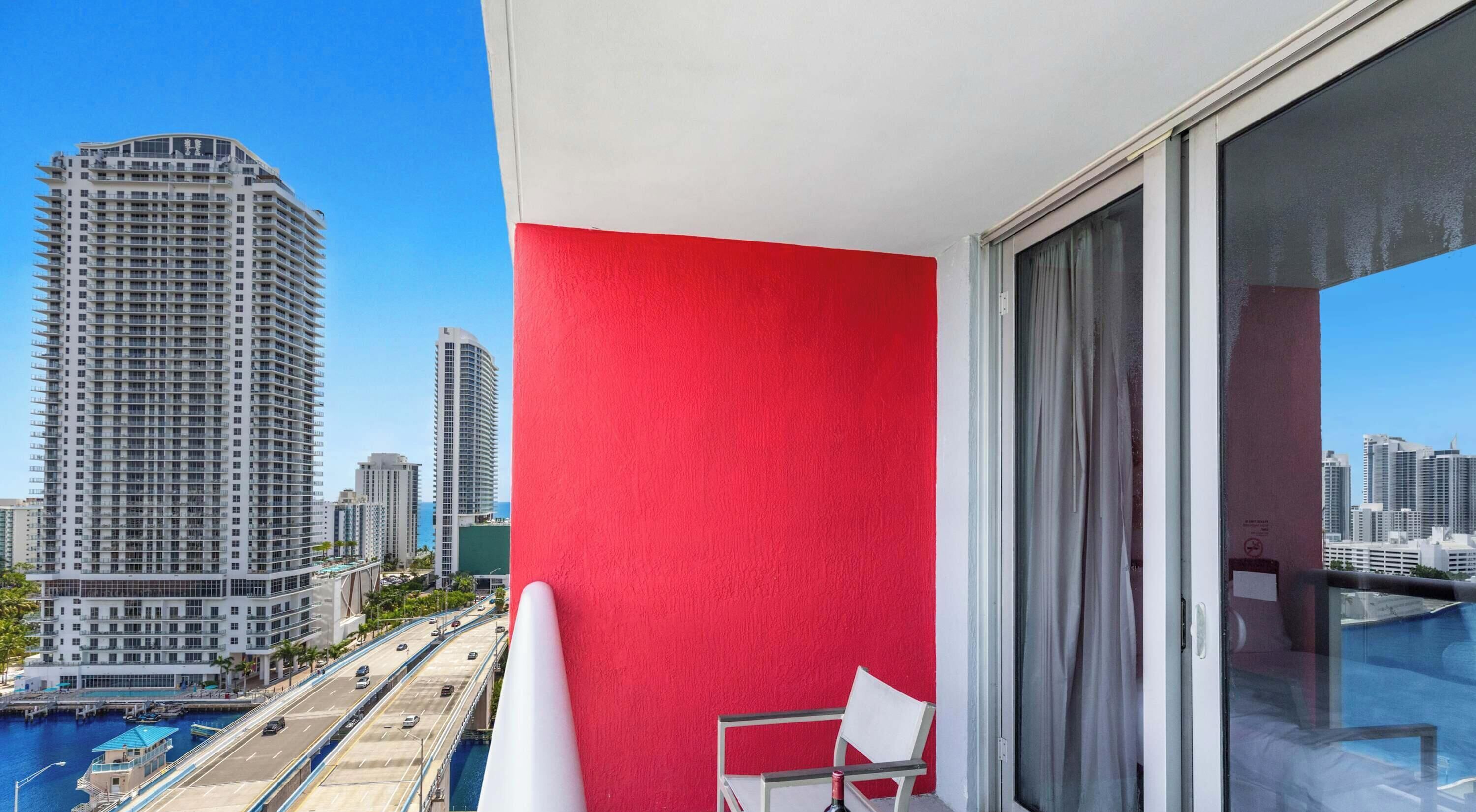 Een balkon met een rode muur, een stoel en uitzicht op een stadsbeeld met hoge gebouwen.