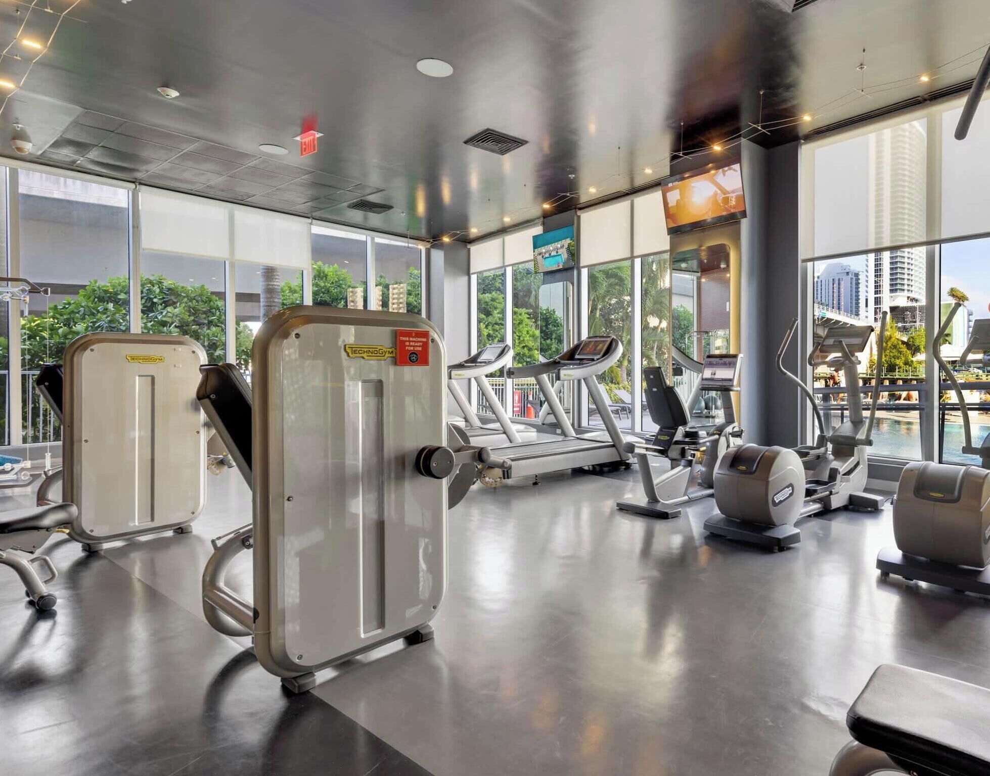 A gym with cardio machines, weight machines, and a large window offering a view of the city.