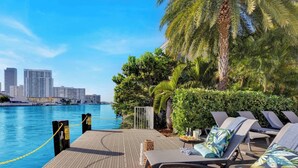 Un área de descanso frente al agua con sillones, una piscina y un horizonte urbano de fondo.