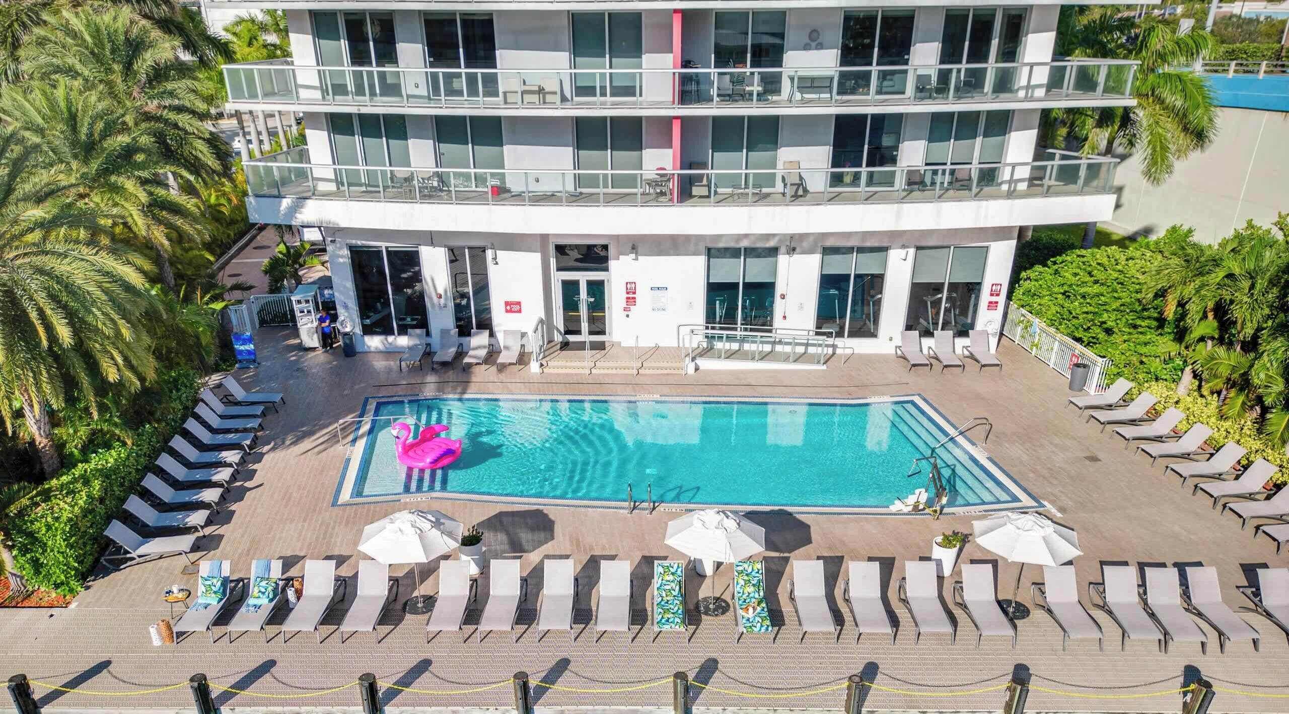 A multi-story hotel with a pool area, including lounge chairs and umbrellas.