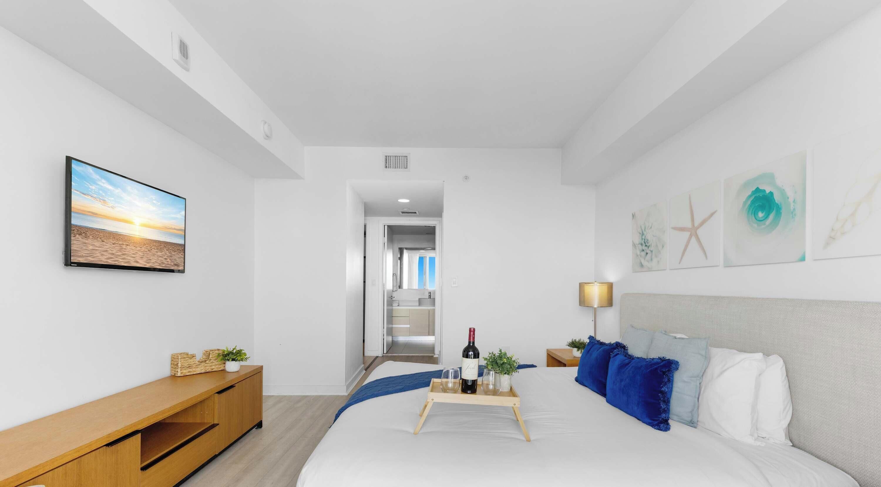 A modern hotel room with a bed, a TV, a wooden console, and artwork on the walls.